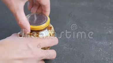 人用蜂蜜把一罐坚果盖上. 双手特写..