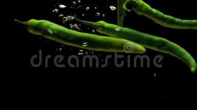 绿色辣椒在黑色背景下落入透明水