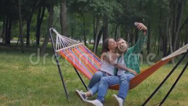 年轻夫妇带着手机坐在吊床上。 从吊床掉到草地上