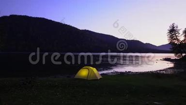 阿尔泰。 黄色帐篷在山湖畔花费.. 晚安。 在帐篷里，光线燃烧。 一个有两个视频