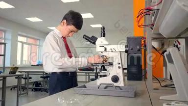 中学男生在显微镜下在学校实验室做生物学研究。