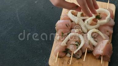 特写女人`她的手把洋葱放在腌制的沙什利克从鸡肉上的木串在木板上，特写。