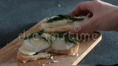 特写女人`她的手拿着一个三明治，里面有面包、黄油、鸡蛋和黑色背景的木板。