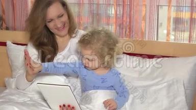 妈妈和可爱的女儿躺在家里的床上，看着数码平板电脑
