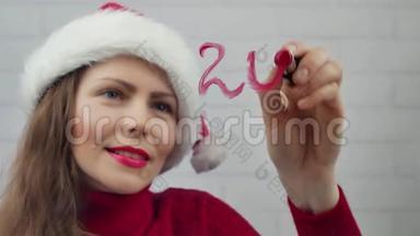 祝2018年新年快乐。 圣诞老人女孩用口红在2018年的玻璃单词上写字。 戴着圣诞帽的漂亮女孩在发信息。