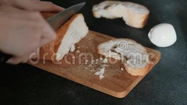 特写女人`她的手在<strong>黑色背景</strong>的<strong>木板</strong>上切一块白面包。 做三明治。
