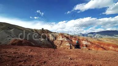 旅行者女孩坐在红山的边缘。 背景中有风景和多云的天空