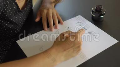 一位年轻女子用刻字技巧在纸上书写书法的特写镜头。 她写着<strong>梦</strong>想远大的目标