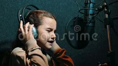 在专业录音室用耳机录制<strong>歌曲</strong>的年轻<strong>女孩</strong>。小<strong>女孩</strong>在唱一首歌
