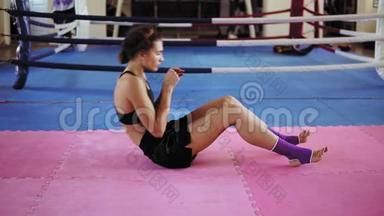 女子拳击手在健身房的训练：年轻中的年轻女子在健身房的拳击场内做腹部按摩