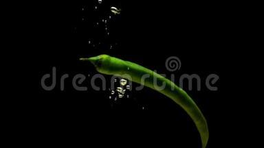 绿色辣椒在黑色背景下落入透明水