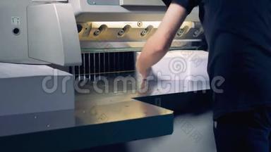 一名员工正在一台切割机下调整两大堆纸张，将它们分成四部分犁出
