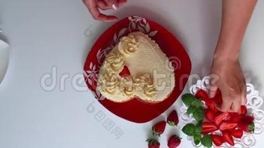 一个女人正在用草莓装饰一块涂满奶油的饼干。 <strong>碟子</strong>旁边是一个切片草莓。