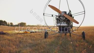 汽车滑翔伞在日落时分用木制螺旋桨站在田野里，飞行员伸出降落伞，