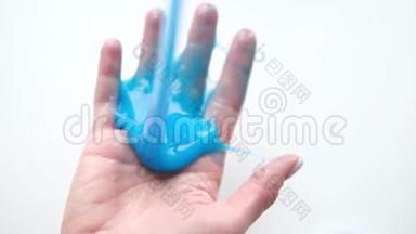 女孩把蓝色的黏液伸到两边。 女人的手在玩黏液<strong>玩具</strong>。 在白色上<strong>做</strong>黏液。 时髦的液体<strong>玩具</strong>棒