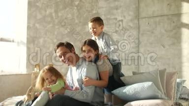 三个孩子和一个年轻的父亲拥抱坐在床上。 家人的早晨。 快乐的父亲。 父亲节`