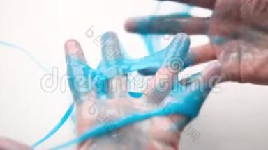 女孩把蓝色的黏液伸到两边。 女人的手在玩黏液<strong>玩具</strong>。 在白色上<strong>做</strong>黏液。 时髦的液体<strong>玩具</strong>棒