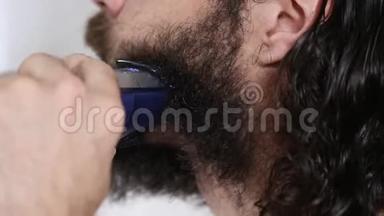 英俊的年轻人留着长发，在浴室里用<strong>修剪器</strong>刮胡子。 特写镜头。