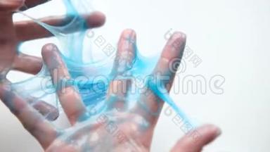 女孩把蓝色的黏液伸到两边。 女人的手在玩黏液玩具。 在白色上做黏液。 时髦的液体玩具棒