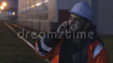 年轻快乐的工人戴着安全帽，晚上通过电话交谈。 4k