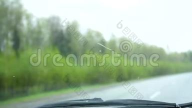 汽车在高速公路上行驶。 外面雨下得很大，挡风玻璃雨刷在工作。 玻璃上的雨滴