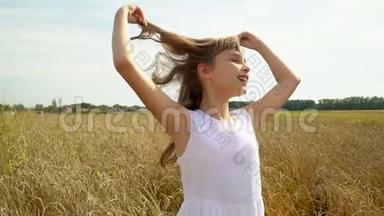 穿着白色连衣裙的女孩穿过金色小麦的田野。 这个美丽的女孩喜欢俄罗斯的开放空间