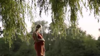 儿子跑过去拥抱她怀孕的母亲。 温暖的阳光穿透了树。