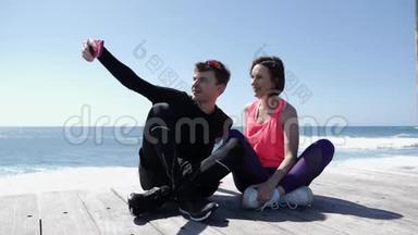 年轻的健康夫妇坐在海滩附近拿着电话，摆出自拍姿势。 快乐的<strong>男朋友</strong>和<strong>女友</strong>拍照