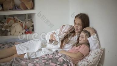 一个小女孩和妈妈躺在床上，看着智能手机屏幕上的<strong>卡通片</strong>、儿童和数字