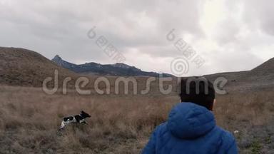 一个男孩带着一只狗在雨中跑过田野，跑到山上