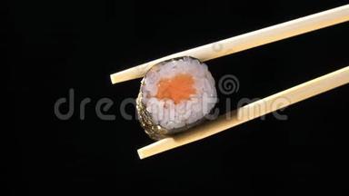 乌黑背景下筷子中的寿司.