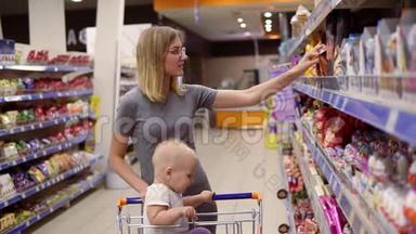 漂亮的年轻妈妈正在超市里挑选糖果和蛋糕，而她的小宝宝正坐在<strong>杂货店里</strong>