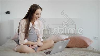 漂亮的黑发女孩正在使用笔记本电脑室内坐在床上。