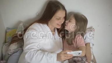 一个小女孩和妈妈躺在床上，看着智能手机<strong>屏幕</strong>上的<strong>卡通</strong>片、儿童和数字