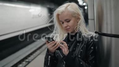 年轻的金发旅行女人手里拿着手机在火车站台上等着。 <strong>公共交通</strong>。