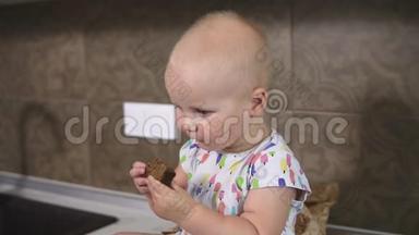 一个可爱的小宝宝吃一块面包。 小可爱的婴儿吃面包，坐在厨房里。 慢镜头