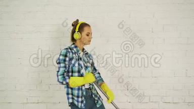 一位带着耳机和拖把的年轻女子准备回家打扫卫生。 为美妙的音乐跳舞唱歌