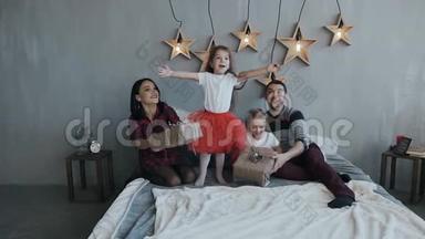这个迷人的家庭正在床上的卧室里玩<strong>圣诞夜</strong>。 穿红色裙子的女孩在床上跳