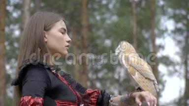 一只浅棕色的猫头鹰坐在一个女人`手上，<strong>展开</strong>翅膀，检查森林