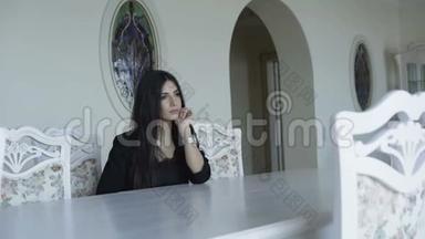 迷人的女人坐在豪华的家中的桌子前摆姿势。