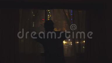年轻人跑到窗户边，打开窗帘，欣赏夜晚从窗户上看到的风景。 4k，3840x2160