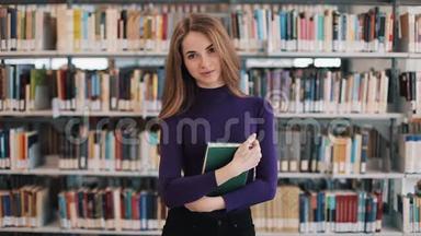 微笑的女学生拿着一<strong>本书</strong>站在图书馆的书架前