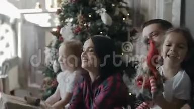 幸福的家庭在家里庆祝圣诞节。 年轻的一家人坐在圣诞树旁边的地板上，兴高采烈