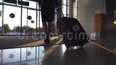 商务小姐带着行李从机场出发。 穿高跟鞋的女人带着她的手提箱从终点站走到城市街道