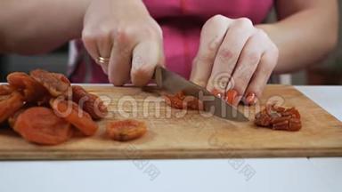 一位年轻的家庭主妇用一把刀在砧板上切果干杏子. 健康饮食观念