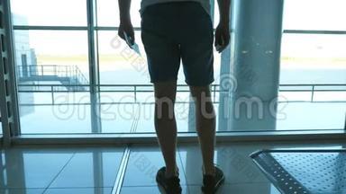 年轻人站在机场候机楼看着窗户。 他在等飞机。 后仰视图