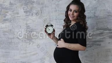 的<strong>孕妇</strong>手里拿着一个钟.. 未来<strong>母亲</strong>的美丽肖像。 等待孩子的女人，宝贝