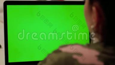 穿<strong>迷彩服</strong>的女孩用绿色屏幕在笔记本电脑上打视频电话