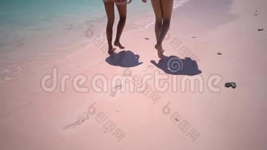 慢动作两个女孩<strong>踩</strong>着他们的<strong>脚印</strong>在粉红色的沙滩上，把漂亮的晒黑的腿贴在粉红色的沙滩上