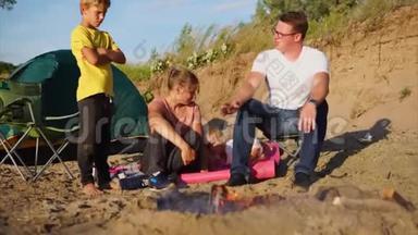 一个有孩子的小家庭在火灾周围取暖，夏天在大自然上搭帐篷